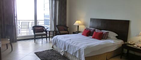 A hotel room with a bed, two chairs, a nightstand, a lamp, and a view of the outside.