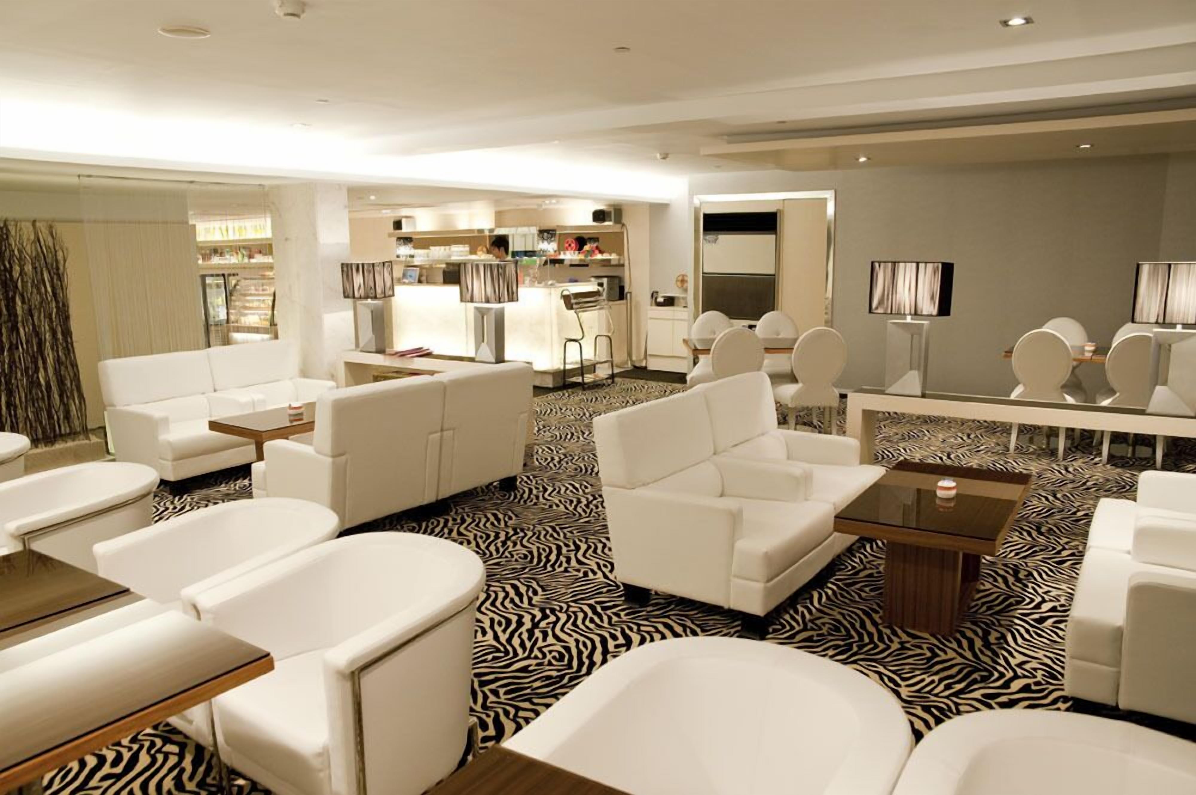 A modern hotel lobby with white sofas, a zebra-patterned floor, and a kitchen area in the background.