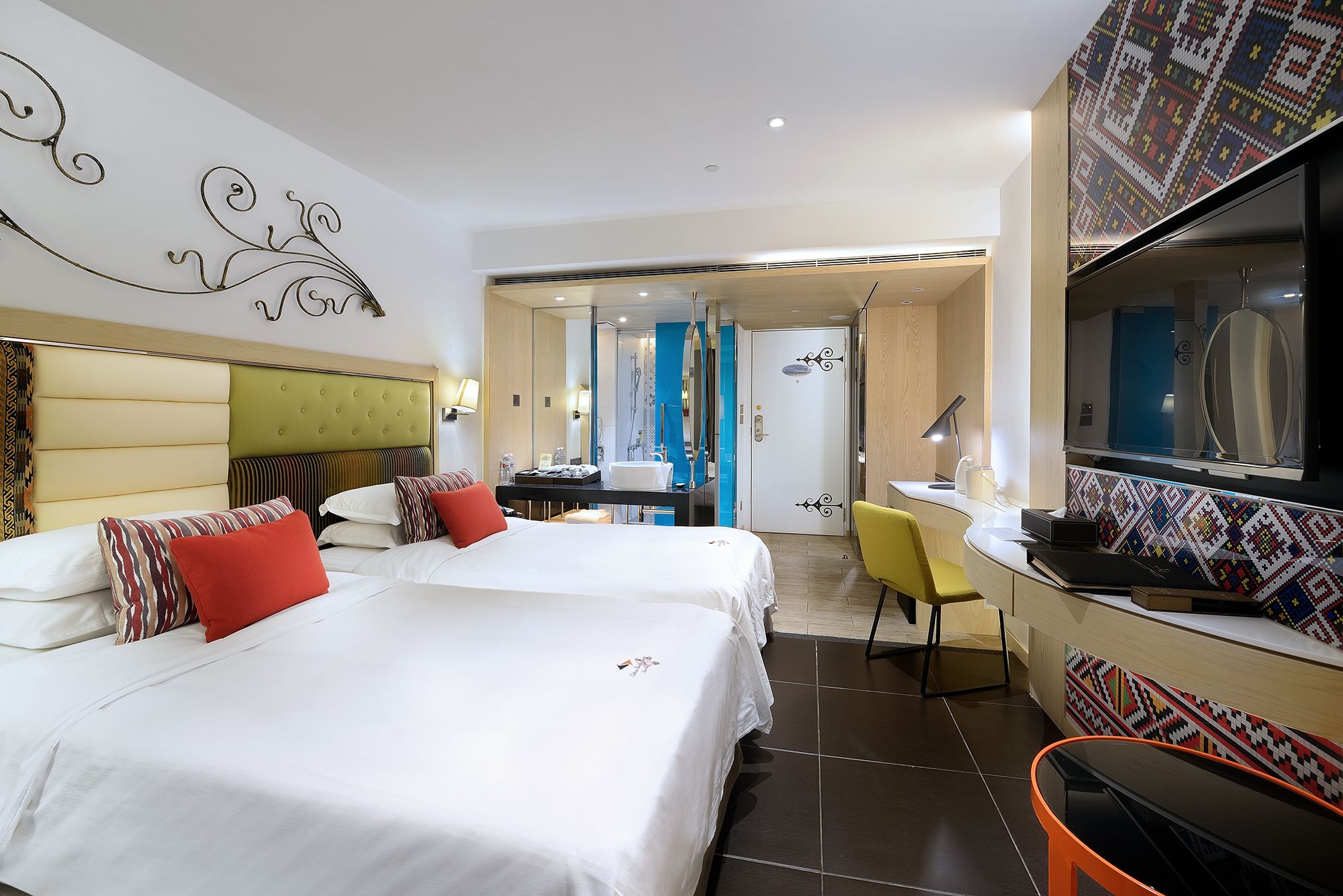 A hotel room with two beds, a desk, a chair, and a TV.