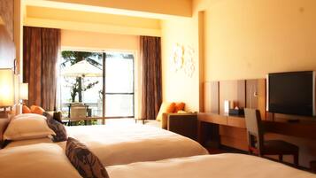 A hotel room with two beds, a desk with a TV, a chair, and a balcony with a table and umbrella.