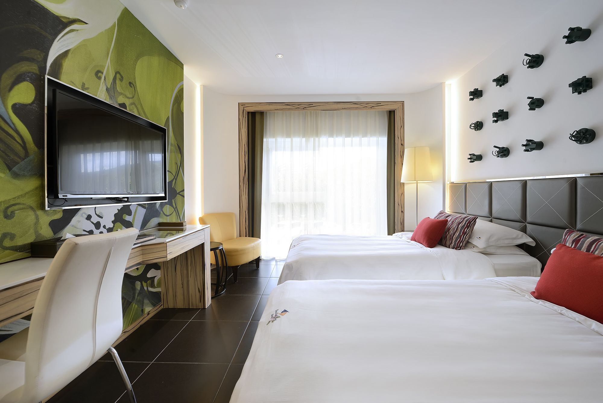 Habitación de hotel con cama, escritorio con televisor, silla y ventana con cortinas.