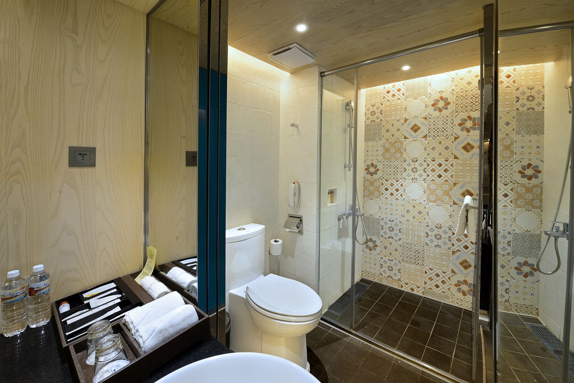 Un baño moderno con cabina de ducha de vidrio, inodoro y zona de lavamanos con toallas y artículos de aseo.