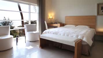 A modern hotel room with a large bed, a desk with a lamp, a chair, and a view of the outdoors.