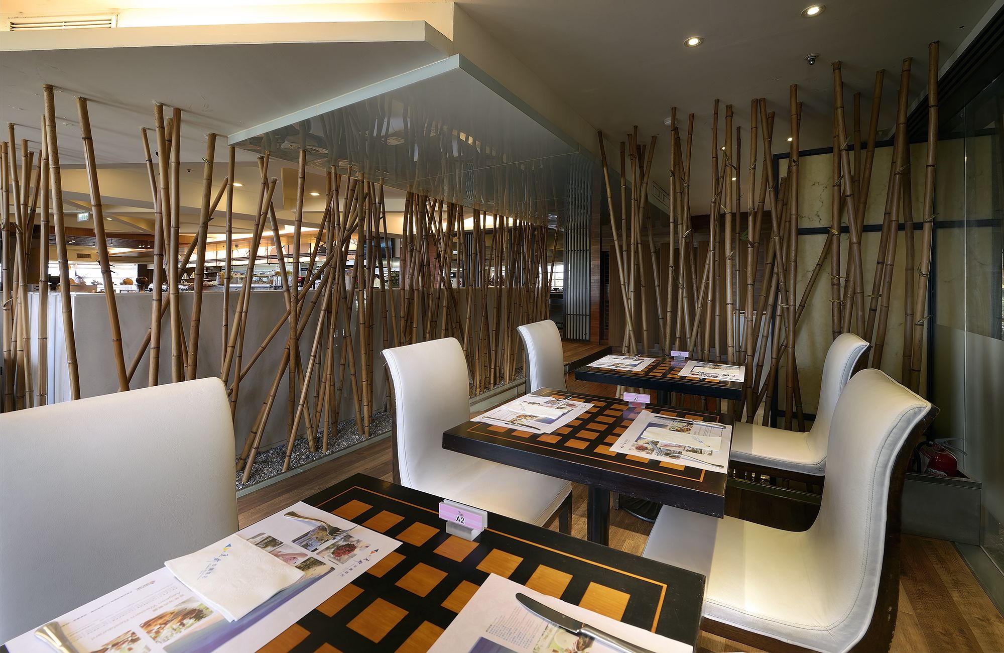 A modern restaurant with bamboo partitions, white leather chairs, and checkered tablecloths.