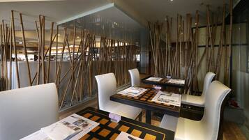 A modern restaurant with bamboo partitions, white leather chairs, and checkered tablecloths.