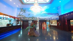 Rebuda d'hotel amb una taulell de recepció, un penjall gran i un mural d'un paisatge tropical.