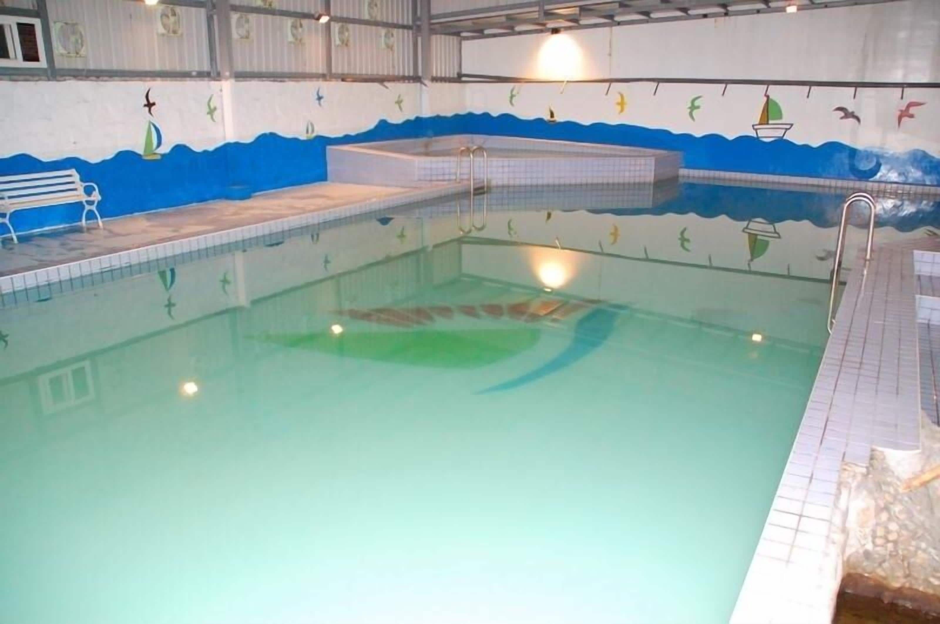 An indoor swimming pool with a tiled floor, a bench, and a mural with sea creatures.