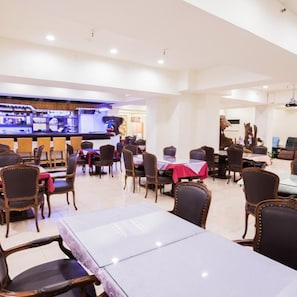 Un restaurante amplio con varias mesas y sillas, una zona de bar y vistas a la ciudad.