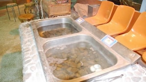 Un dispositiu de bufet amb dues safates metàl·liques plenes d'aliments, tot envoltat de cadires de plàstic taronja.