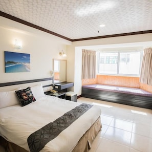 Habitación de hotel con una cama grande, una mesita de noche, una ventana con cortinas y un cuadro en la pared.