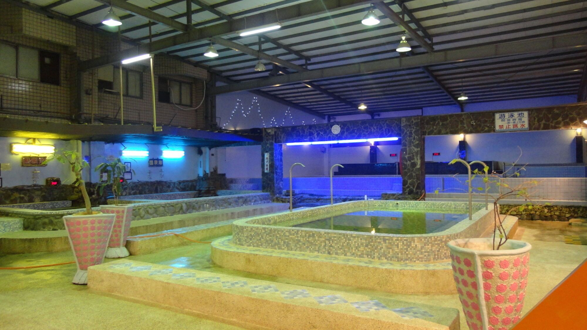 An indoor swimming pool area with multiple pools, steps leading to the pools, and decorative lighting.