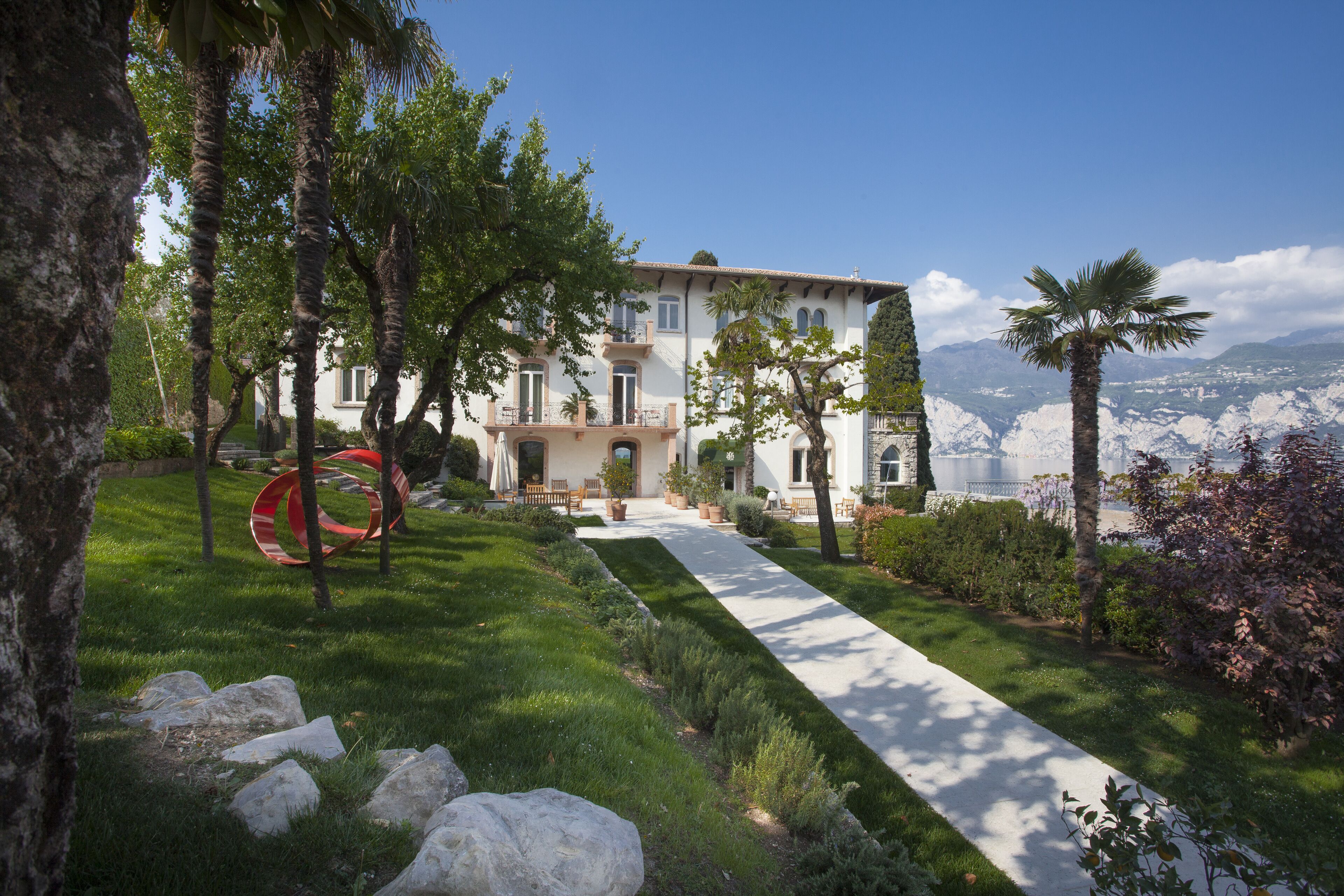 A building with a garden pathway, palm trees, and a view of mountains.