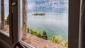 Een kamer met uitzicht op een meer en bergen, te zien door een raam met houten kader en stenen pilaren.