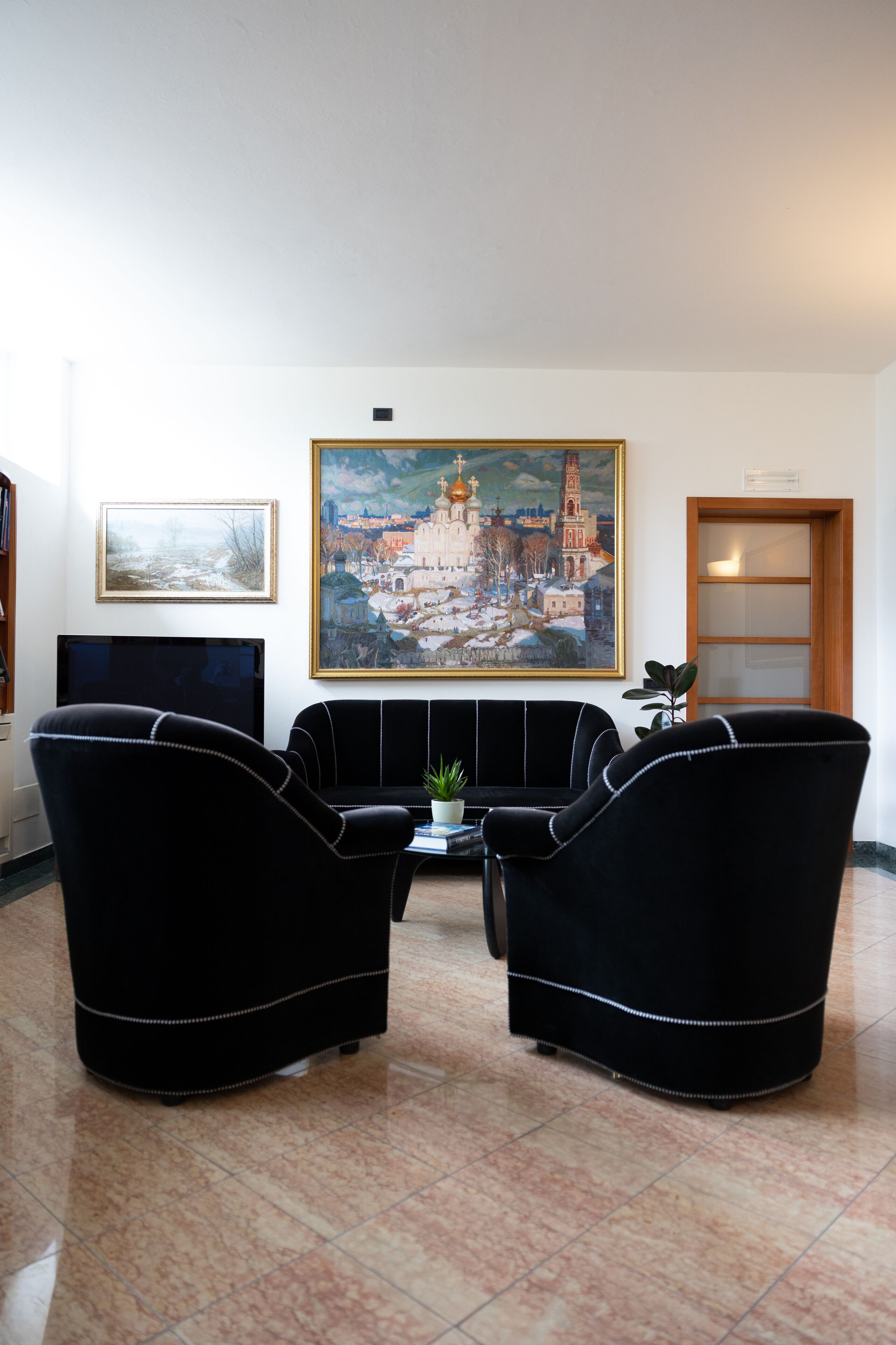 A living room with two black armchairs, a flat-screen TV, a painting, and a wooden door.