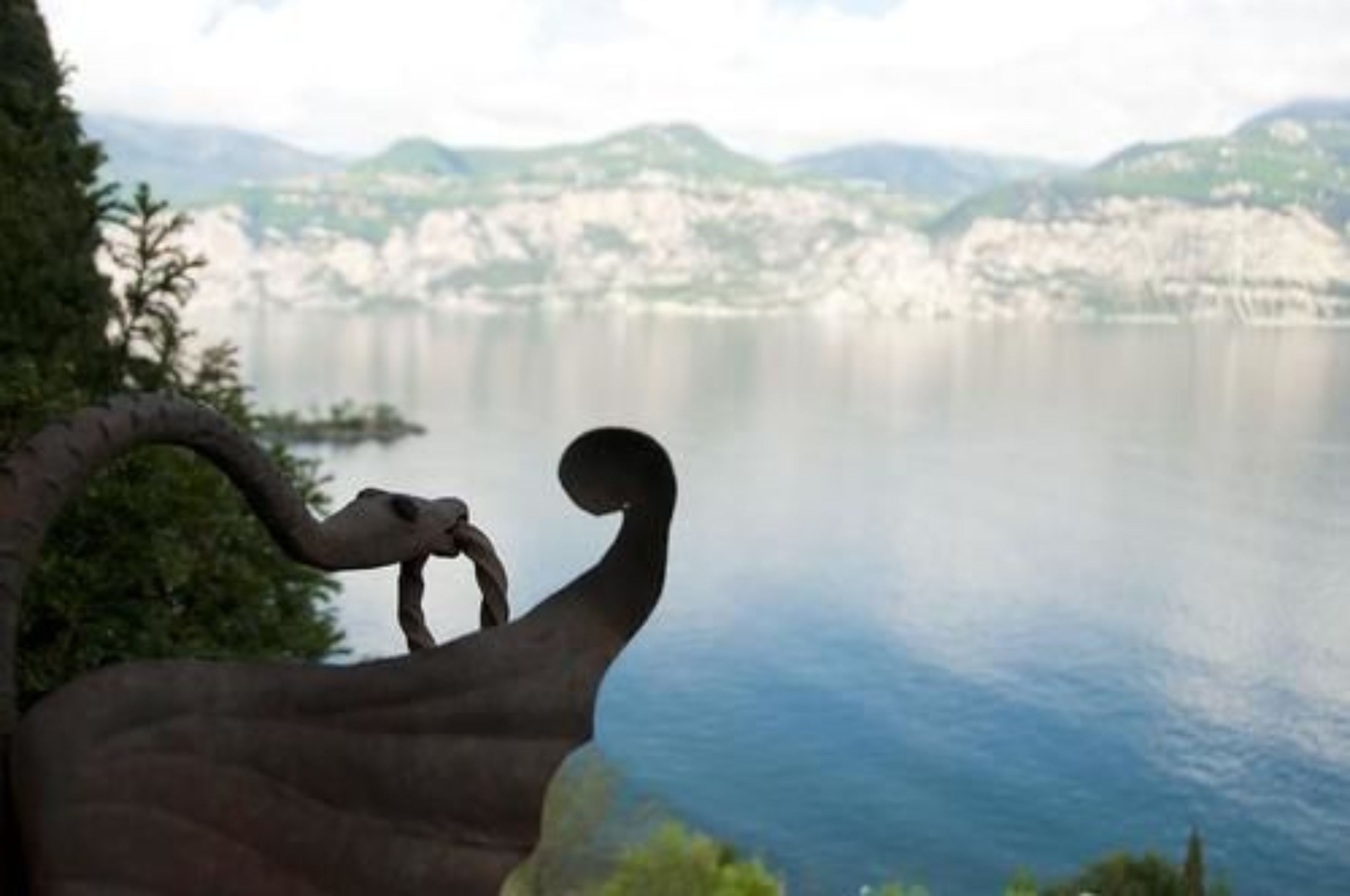 A sculpture of a mythical creature overlooking a lake with mountains in the background.