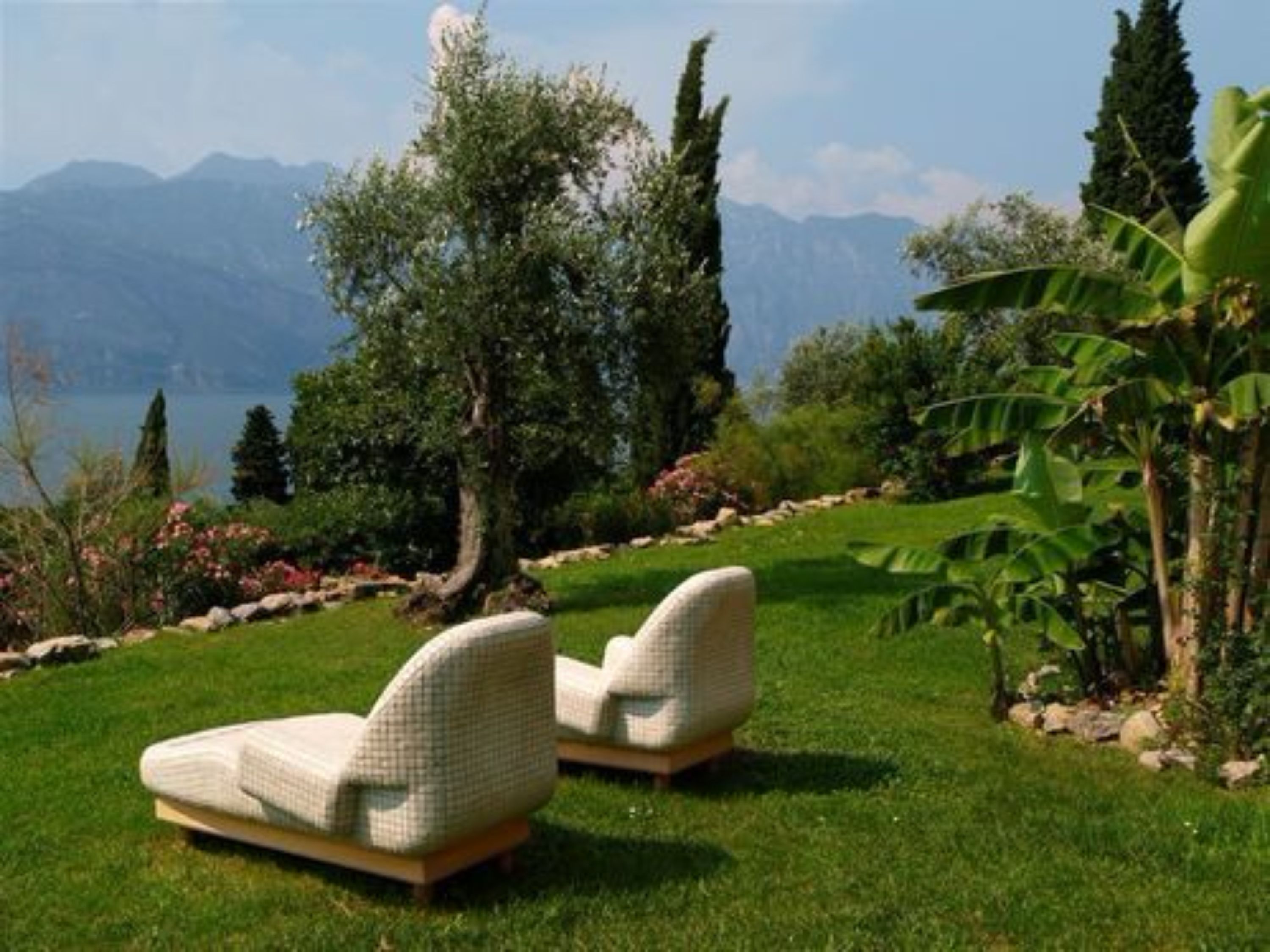 Two outdoor lounge chairs with a view of mountains and a lake.