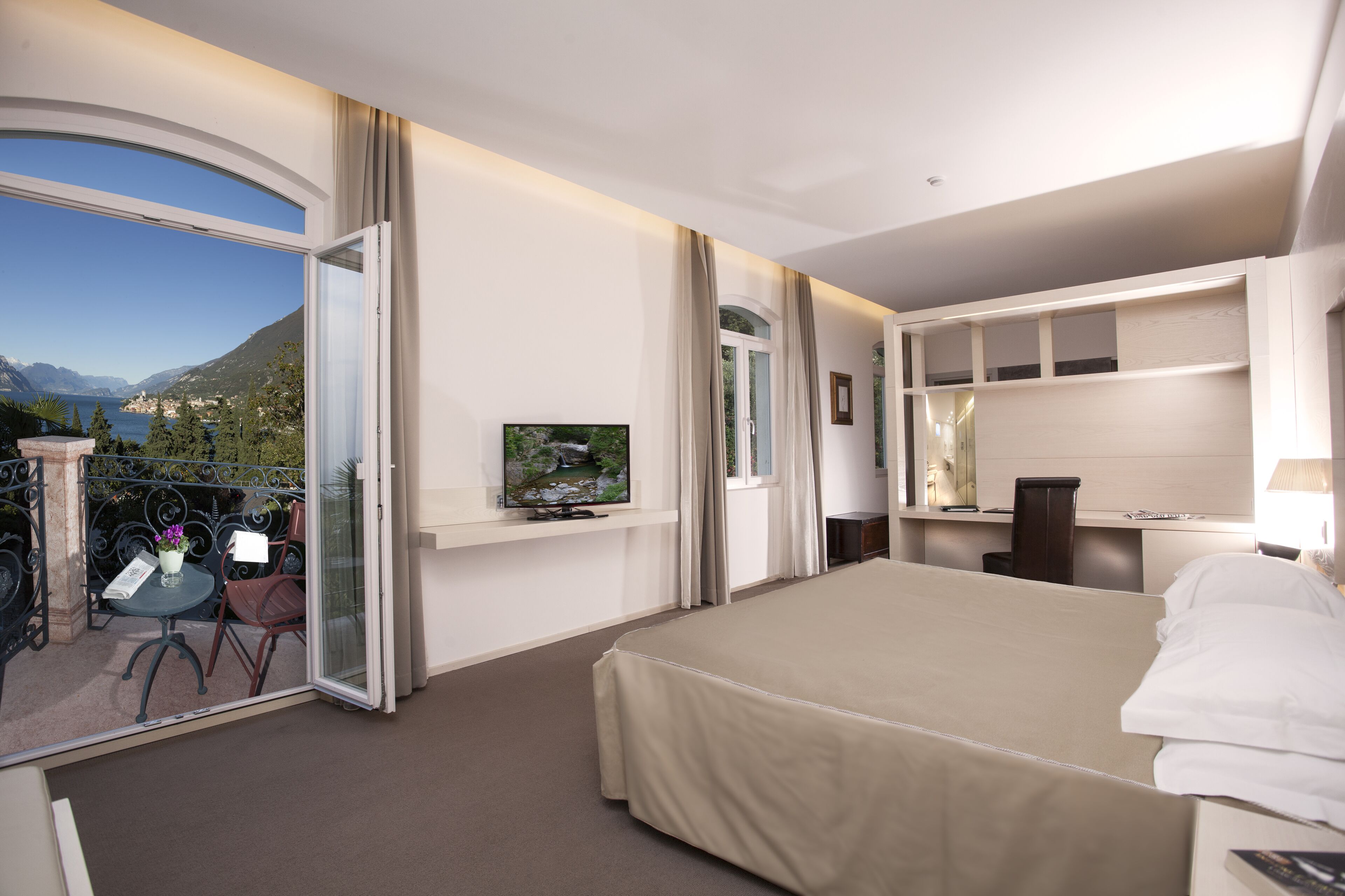 Ein Hotelzimmer mit einem großen Bett, einem Fernseher, einem Schreibtisch und einem Balkon mit Bergblick.