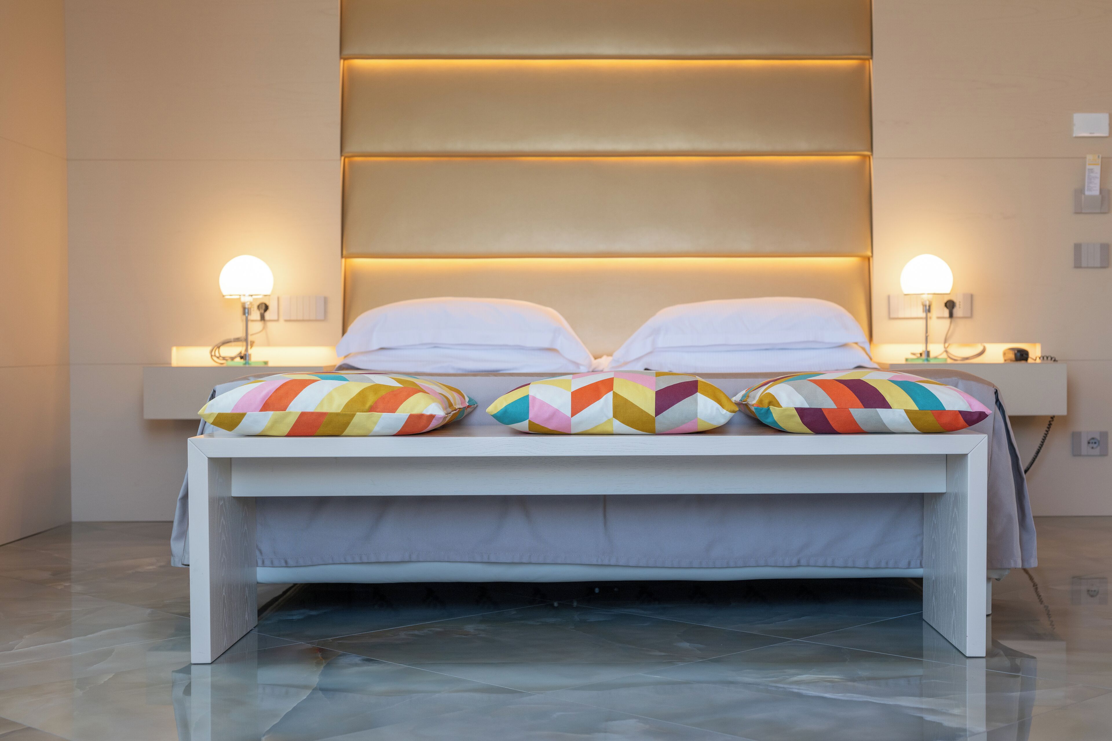 Camera d'albergo moderna con un letto, due lampade da comodino e cuscini colorati.