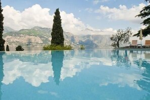 Ein klares Schwimmbecken mit Blick auf die Berge, umgeben von Bäumen und Liegestühlen.