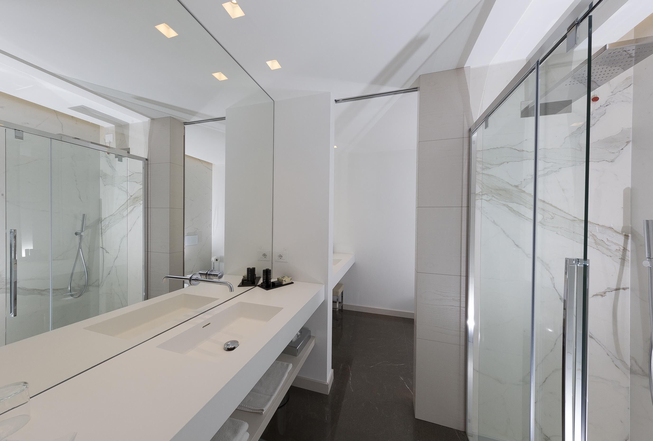 A modern bathroom with a large mirror, a glass shower enclosure, and a marble-tiled floor.