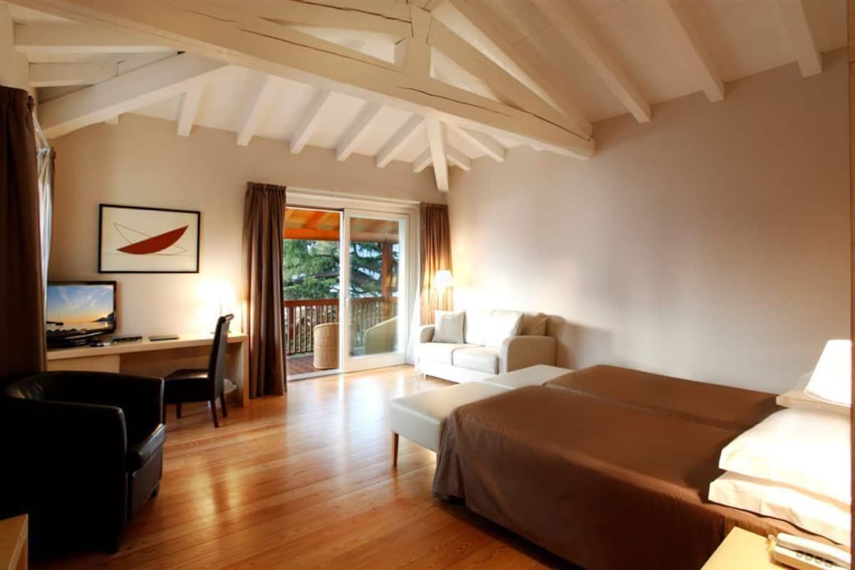 Une chambre d’hôtel avec un plancher en bois, un lit, un bureau avec une chaise, un canapé et un balcon avec des rideaux.
