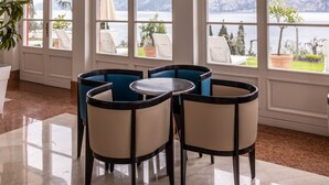 Een ruime kamer met een grote tafel en stoelen, met hoge boogvensters met uitzicht op bergen en een meer.