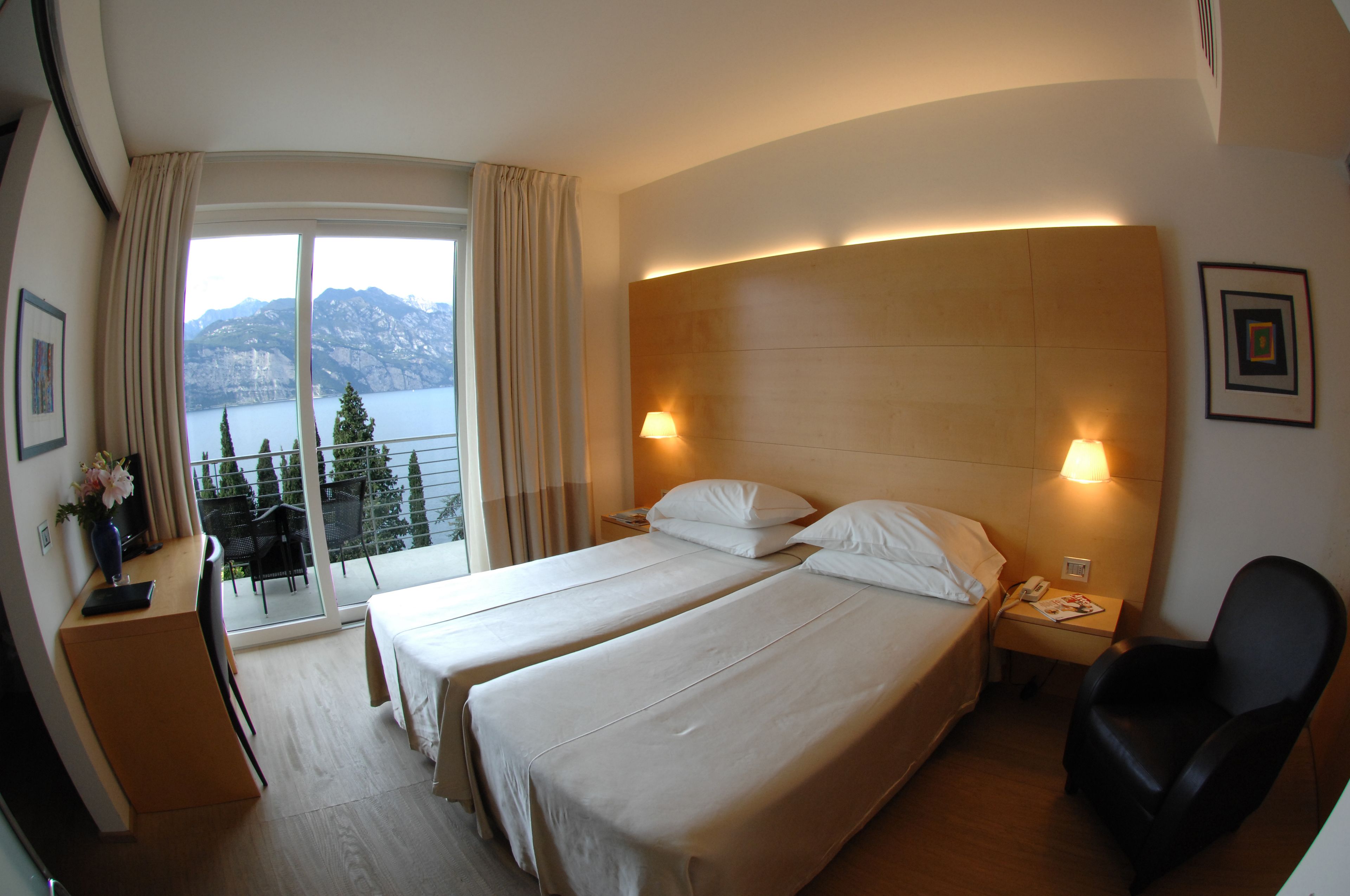 A hotel room with two beds, a desk, a chair, and a view of mountains and water.