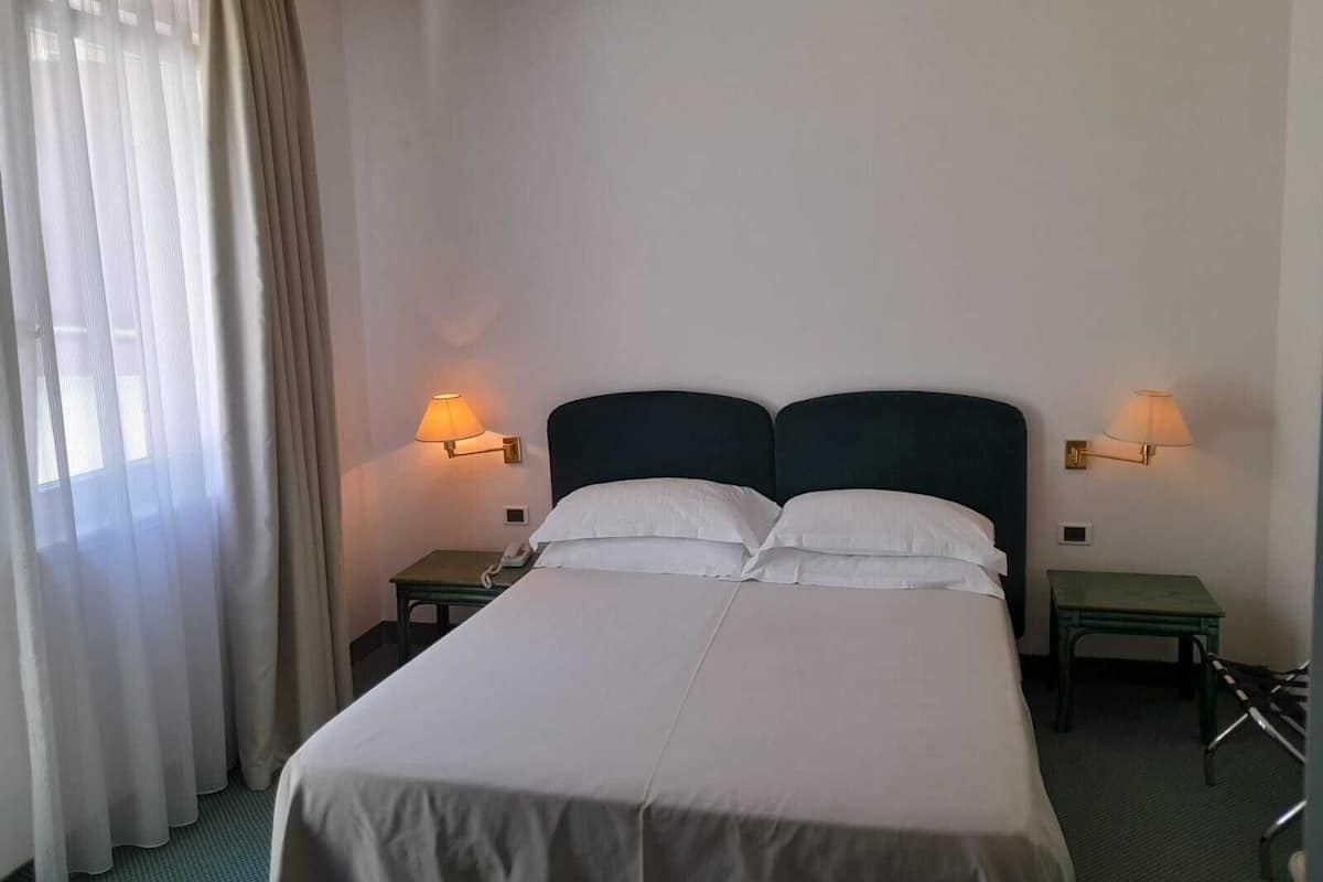 Une chambre d’hôtel avec un grand lit, deux tables de chevet, un téléphone et deux lampes fixées au mur.