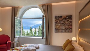 Een hotelkamer met een groot raam, een bed met handdoeken, een rode stoel en een schilderij aan de muur.