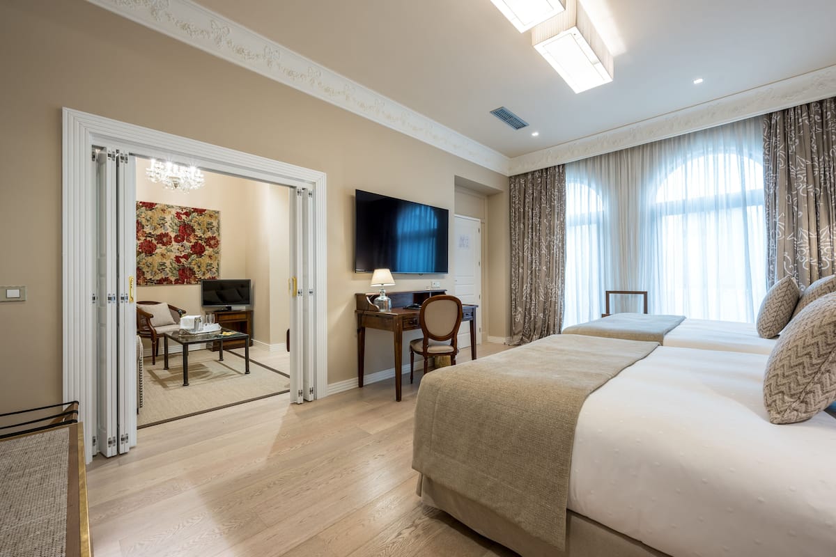 A hotel room with a large bed, a desk with a computer, a TV, and a dining area with a table and chairs.