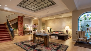 A spacious living area with a wooden staircase, a large stained glass window, and a cozy seating arrangement. - Hotel Rector (Salamanca)