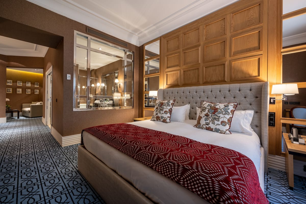 A spacious hotel room with a large bed, a wooden headboard, a large mirror, and a view of the hallway.