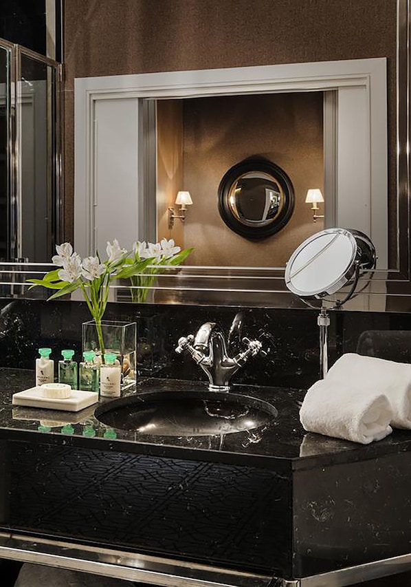 A black marble bathroom vanity with a sink, two wall-mounted mirrors, and a vase of white flowers.