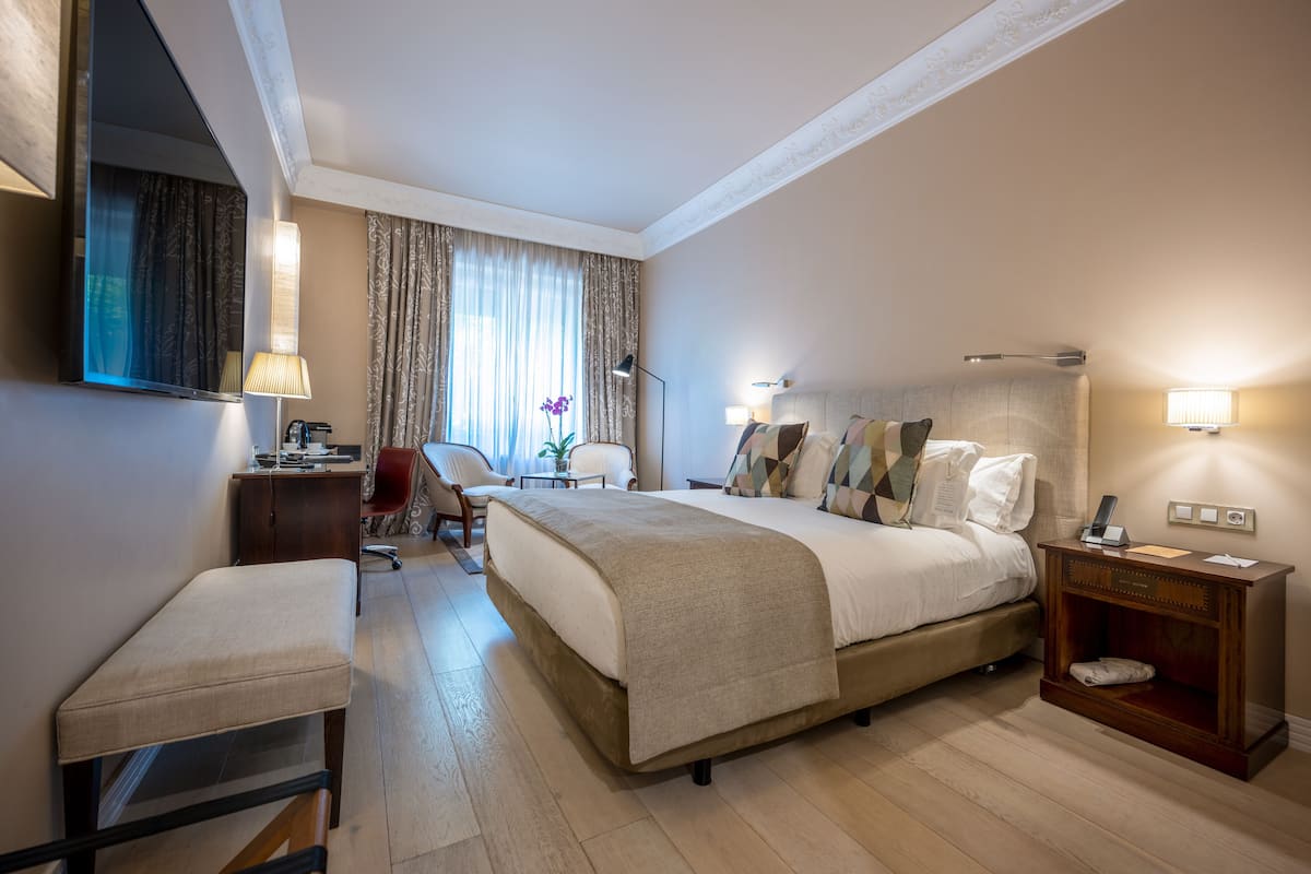A hotel room with a large bed, bedside tables, a desk, a chair, and a mirror.