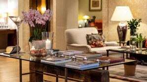 A well-lit, elegantly furnished living room with a glass coffee table, books, candles, and decorative flowers. - Hotel Rector (Salamanca)