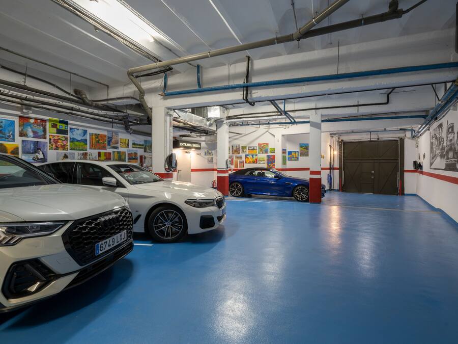 A parking garage with three cars, a blue car, a white car, and a silver car.
