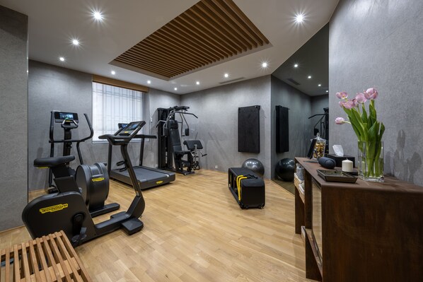 Un gimnasio moderno con diversos equipos de ejercicio, piso de madera y un escritorio con un florero.