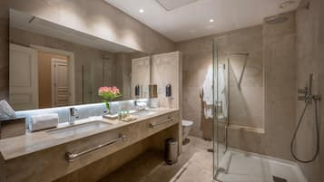 A modern bathroom with a large mirror, two sinks, a glass shower enclosure, and a toilet.