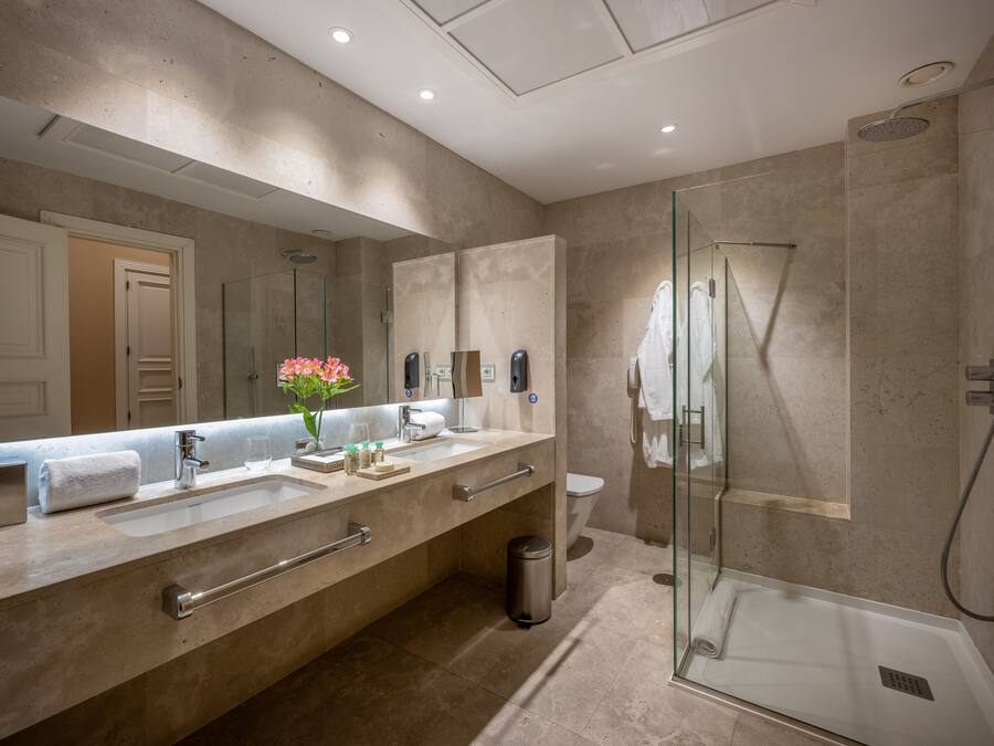 A modern bathroom with a large mirror, two sinks, a glass shower enclosure, and a toilet.