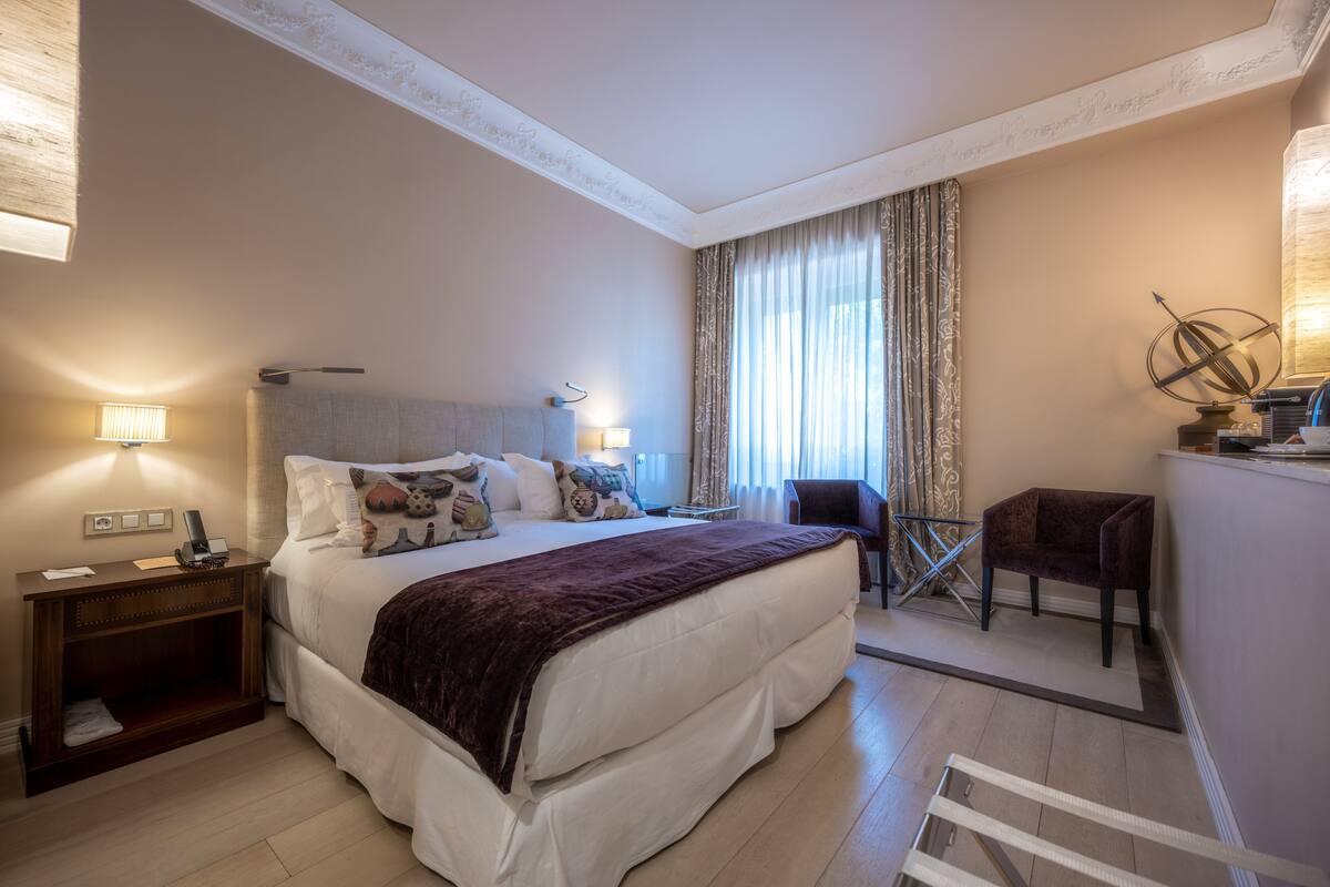 A hotel room with a large bed, a desk, a chair, and a window with curtains.