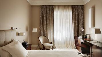 A hotel room with a bed, two chairs, a desk, a lamp, and a large window with curtains.