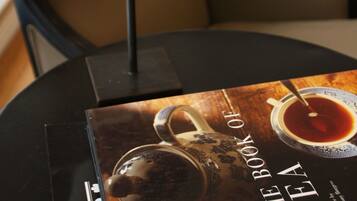 A book titled "The Book of Tea" on a table with a tea set and a lamp.