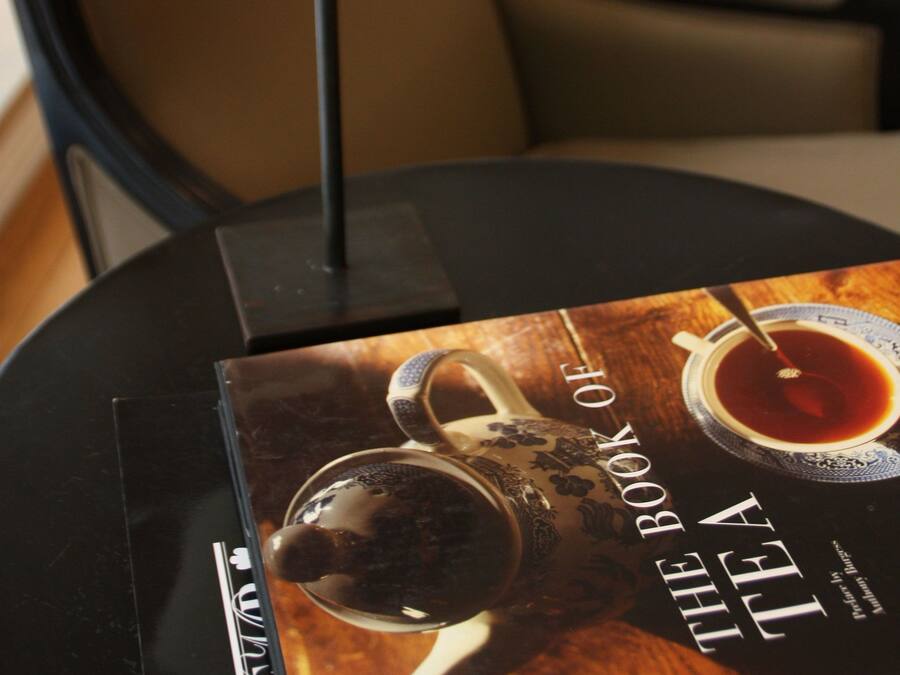 A book titled "The Book of Tea" on a table with a tea set and a lamp.