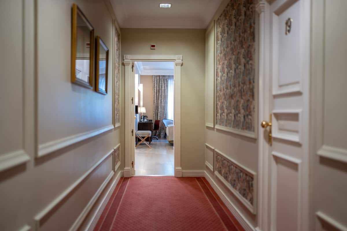 A hallway with a red carpet leading to a room with a bed and a desk.