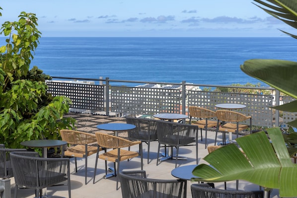 An outdoor patio with wicker chairs and round tables, overlooking a body of water. - Aluasoul Orotava Valley (Puerto de la Cruz)