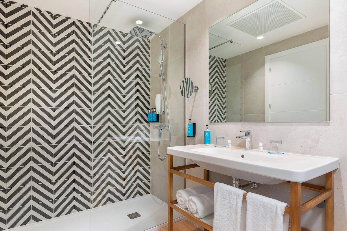 A modern bathroom with a large mirror, a white sink, and a shower area with a chevron-patterned wall.
