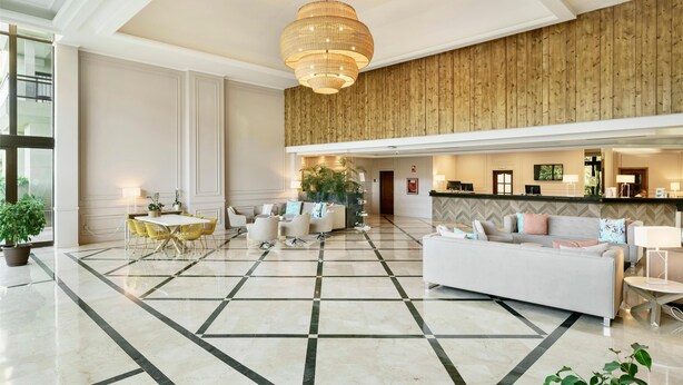 A spacious lobby with a checkered floor, a central seating area with a round table and chairs, a large sofa, and a reception desk. - Aluasoul Orotava Valley (Puerto de la Cruz)