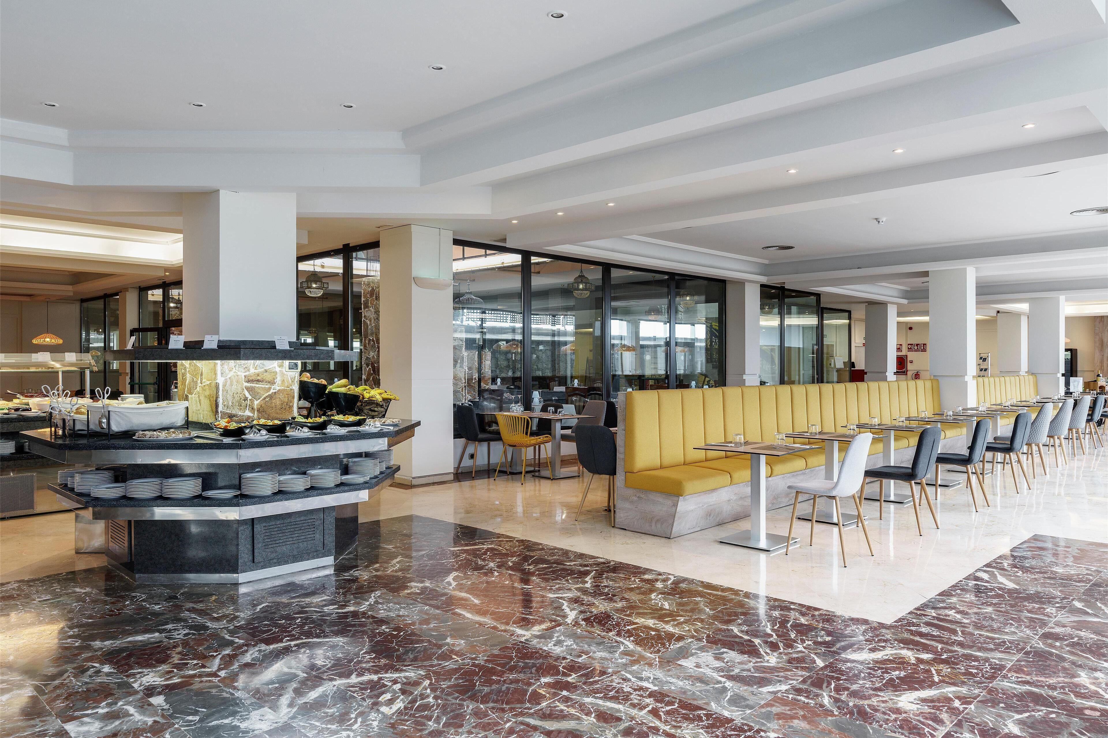 Una hall d'albergo moderna con pavimento in marmo, angolo buffet e sedute gialle.