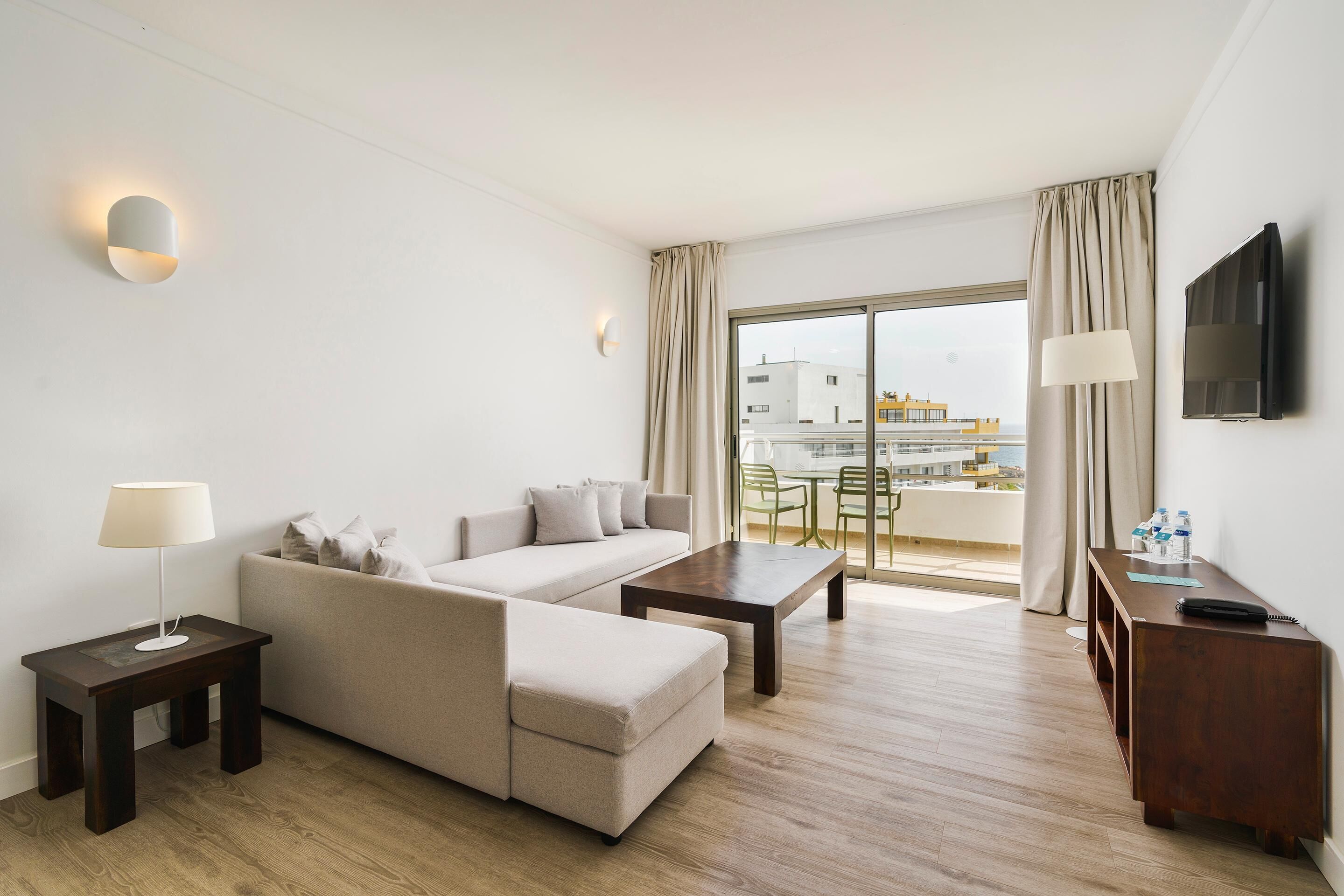 Habitación de hotel moderna con sofá, una mesa de centro, televisión y balcón con vistas a edificios.