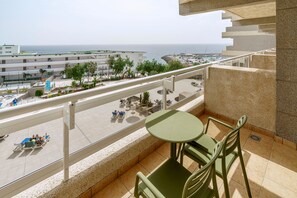 A balcony with a table and chairs, overlooking a beach and a marina with boats.